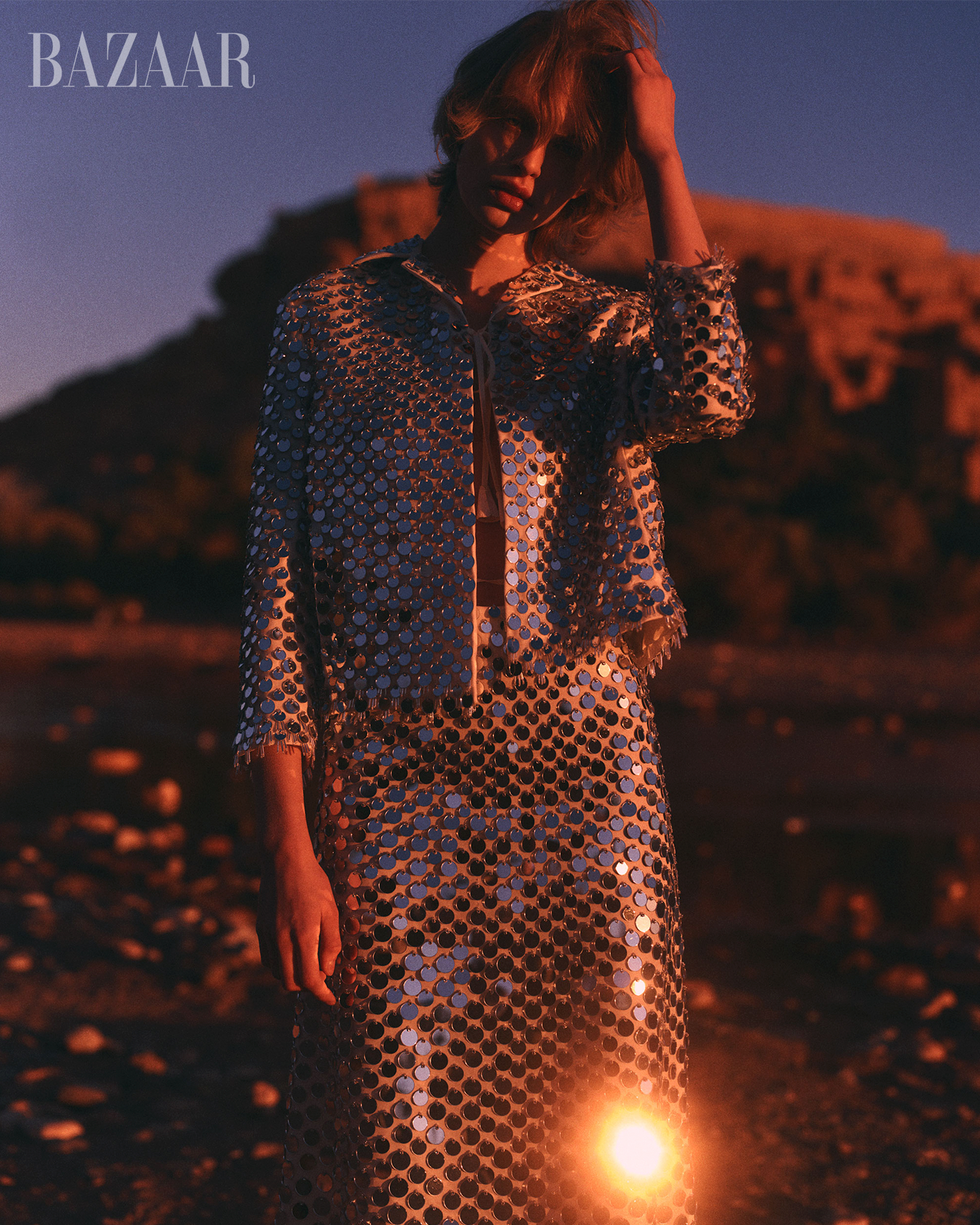 fashion model wearing a reflective sequined outfit against a sunset backdrop
