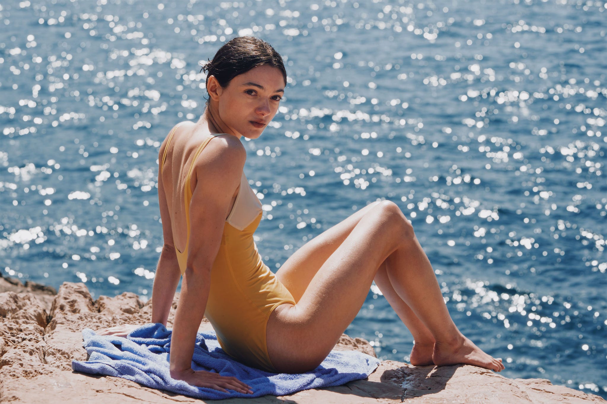person sitting on a rock by the water in a swimsuit