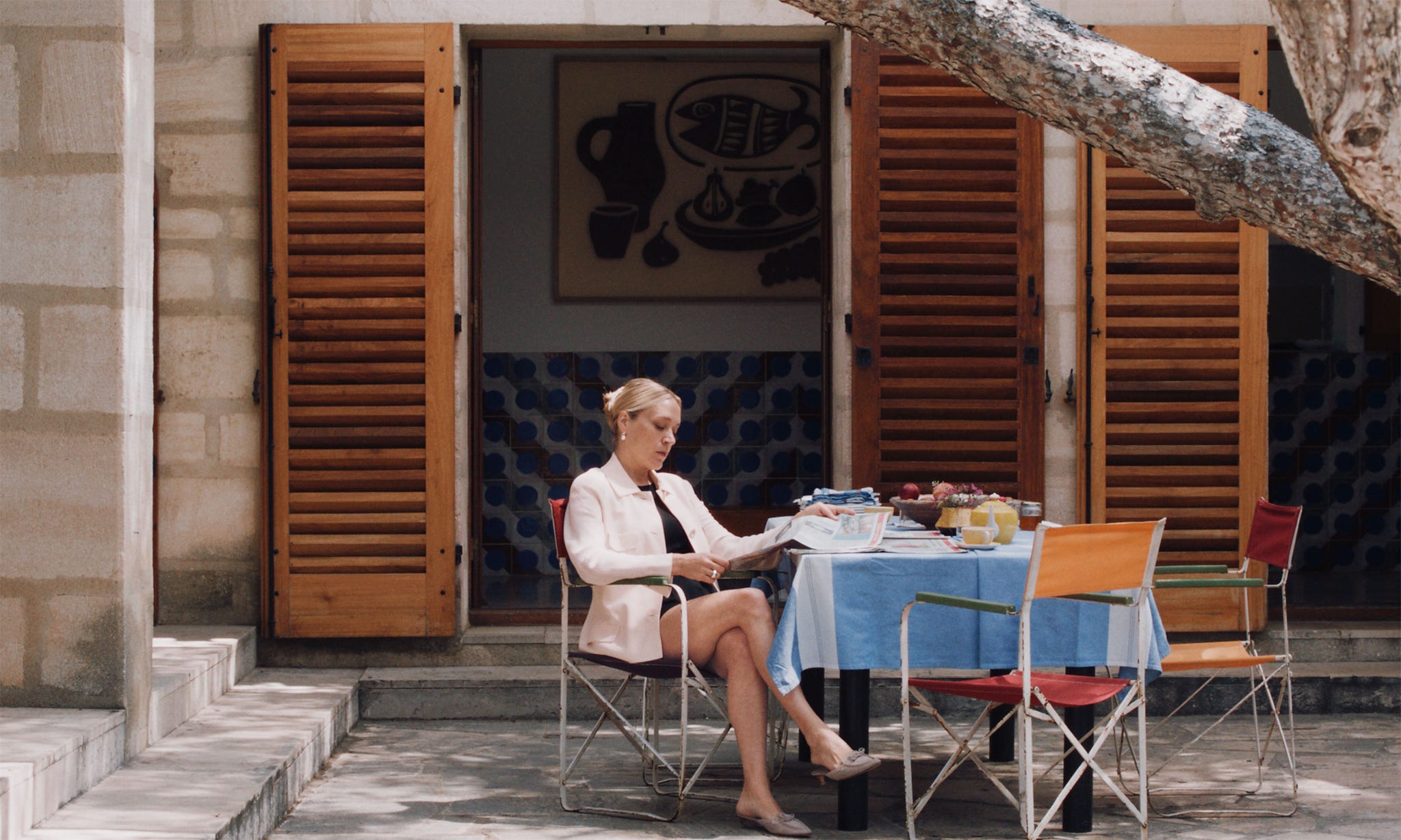 outdoor setting with a woman seated at a table reading surrounded by food items
