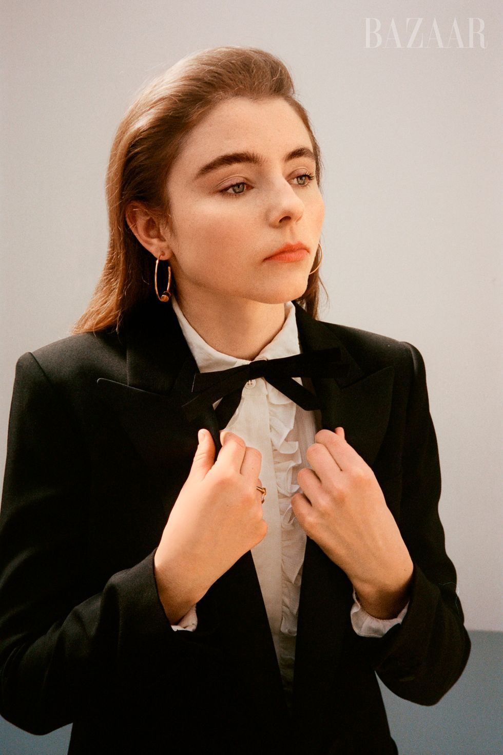 thomasin poses by pulling on lapels of suit jacket