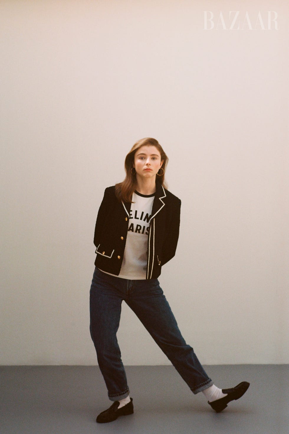 thomasin poses in black and white blazer, a t shirt, jeans, white socks, and black loafers against a white wall