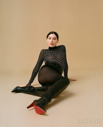 bishop sits in black bodysuit with white polka dots against tan background