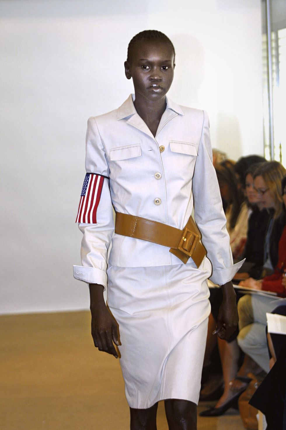alek walks down runway in white jacket and skirt with american flag on sleeve