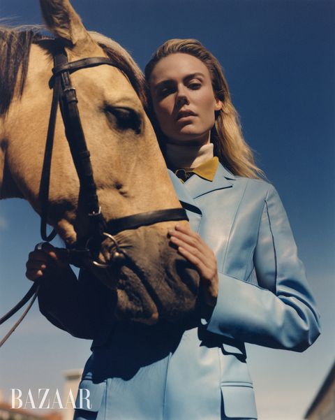 woman in blue coat yellow collar holding horse head