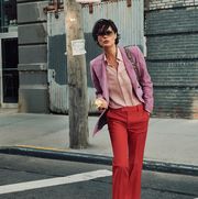 shalom crosses street wearing lavender blazer and pink button up and red trousers