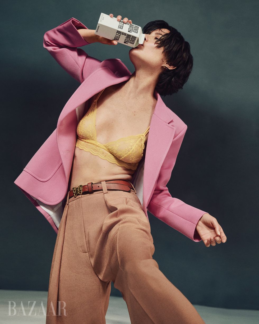 woman in pink blazer brown trousers yellow bralette sipping on boxed water