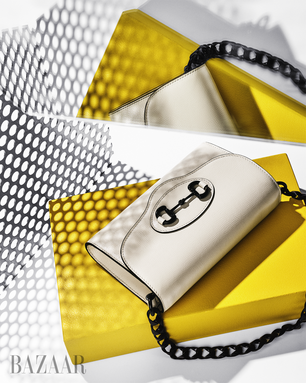 a white gucci bag designed for bloomingdale's 150th anniversary collection shot on top of a yellow box with a graphic black and white background