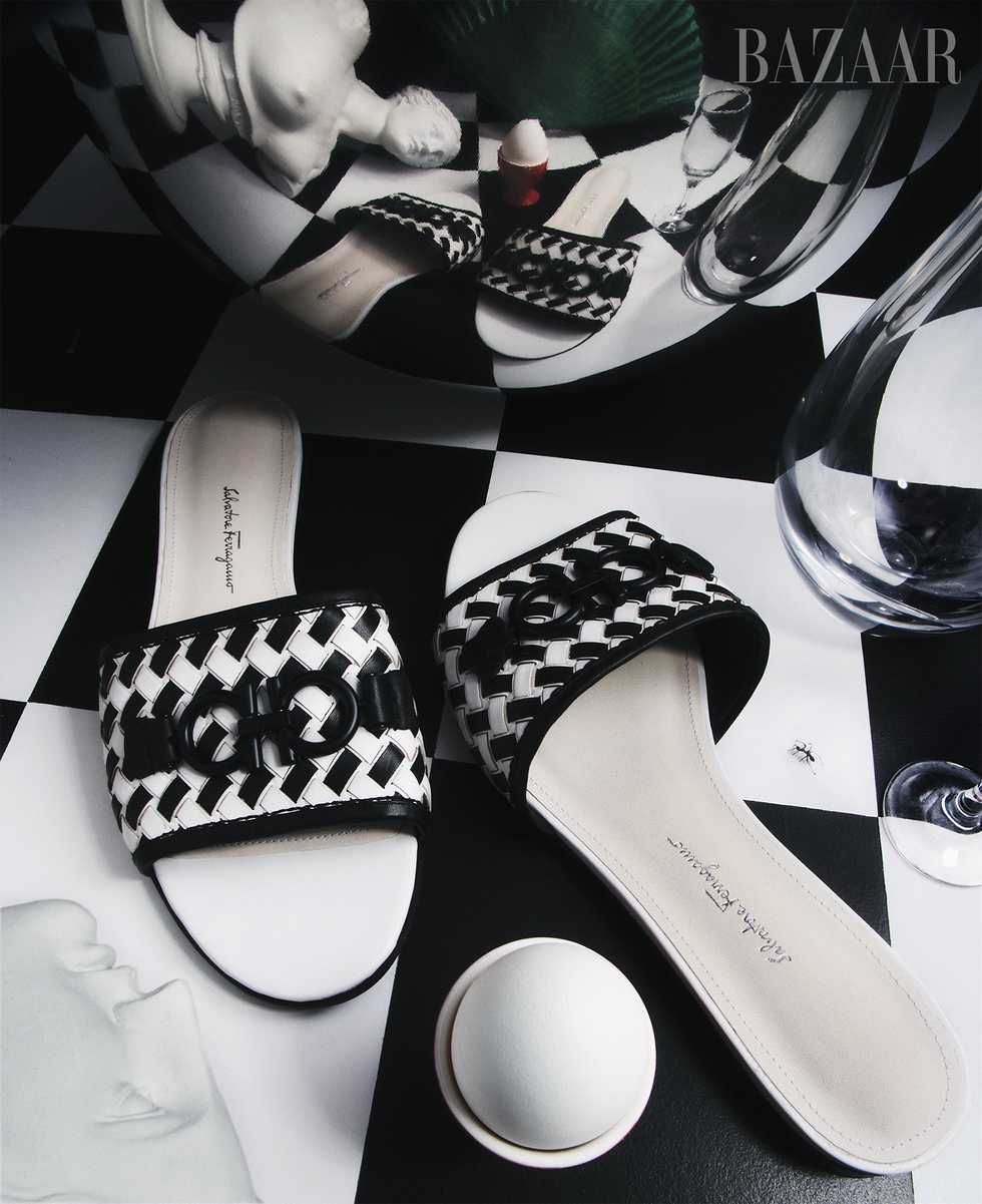 black and white woven flat sandals designed by salvatore ferragamo for bloomingdale's 150th anniversary collection, shot on a black and white checkered floor surrounded by a surreal collection of objects