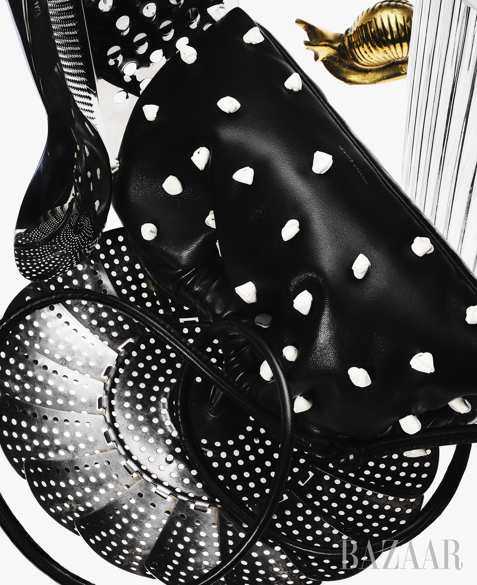 mansur gavriel's mini cloud clutch, in black with white polka dots, designed for bloomingdale's 150th anniversary collection, shot on a surreal black and white background surrounded by kitchen implements and a golden snail
