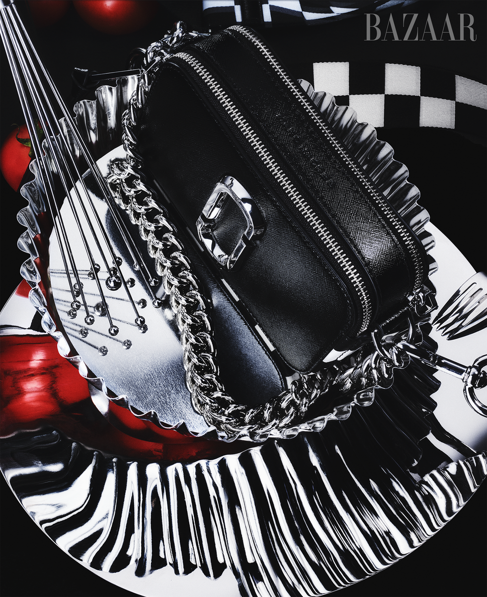 a boxy black marc jacobs bag designed for bloomingdale's 150th anniversary collection, shot on a surreal black and white background surrounded by unidentifiable objects in silver and red