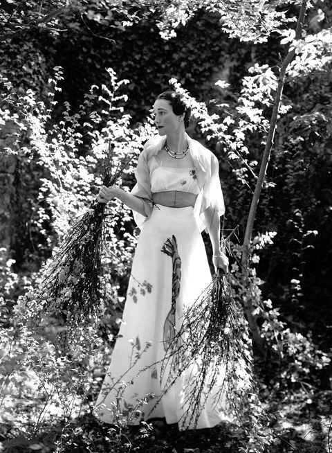 the duchess of windsor wearing a white dress with painted design on the skirt, standing and holding bundles of flowered twigs in the garden of the chateau de cande photo by cecil beaton conde nast via getty images