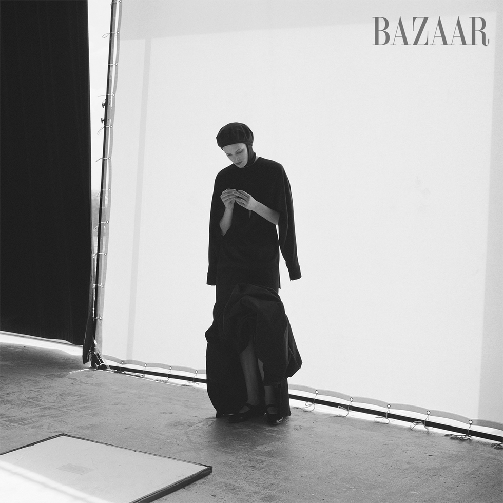 a model wearing a black outfit stands against a light backdrop
