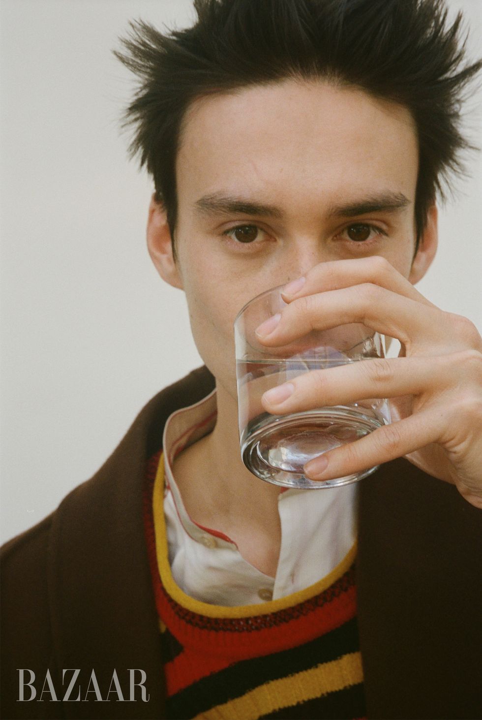 jacob collier drinks from a glass of water while staring directly at the camera