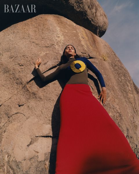 woman in red skirt and blue and brown shirt against rock