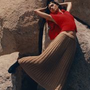 model leans against boulders in a red knit top and a camel knit skirt