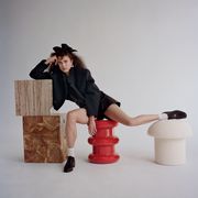 margaret wears a black shorts suit with a black bow in her hair, posing on an assortment of abstract props