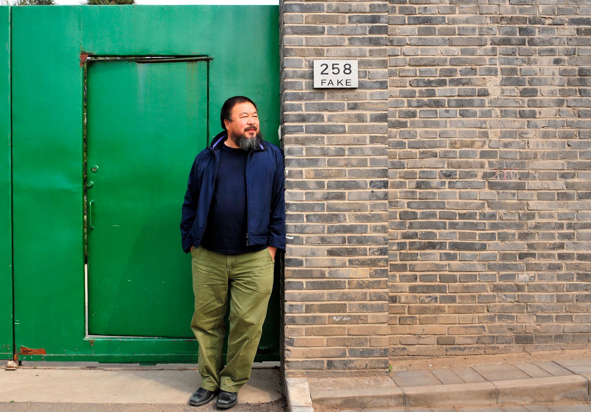 chinese artist ai weiwei stands in front of a green door and brick wall outside of his art studio in caochangdi beijing