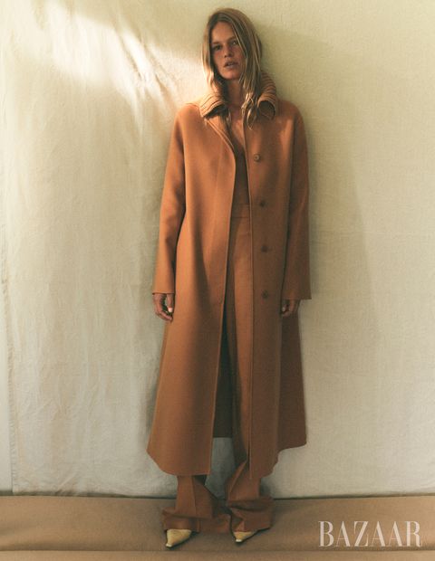 model anna ewers in monochrome tan orange trench coat and trousers and yellow pumps posing against white wall