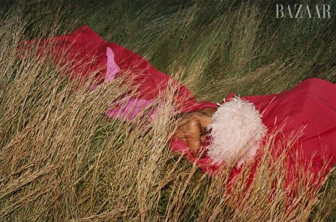 tracee wears fluffy pink hat and hot pink cape gown draped over her while laying down in grass