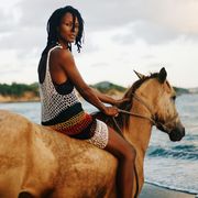 shala monroque looking over shoulder at camera sitting on top of a light brown horse