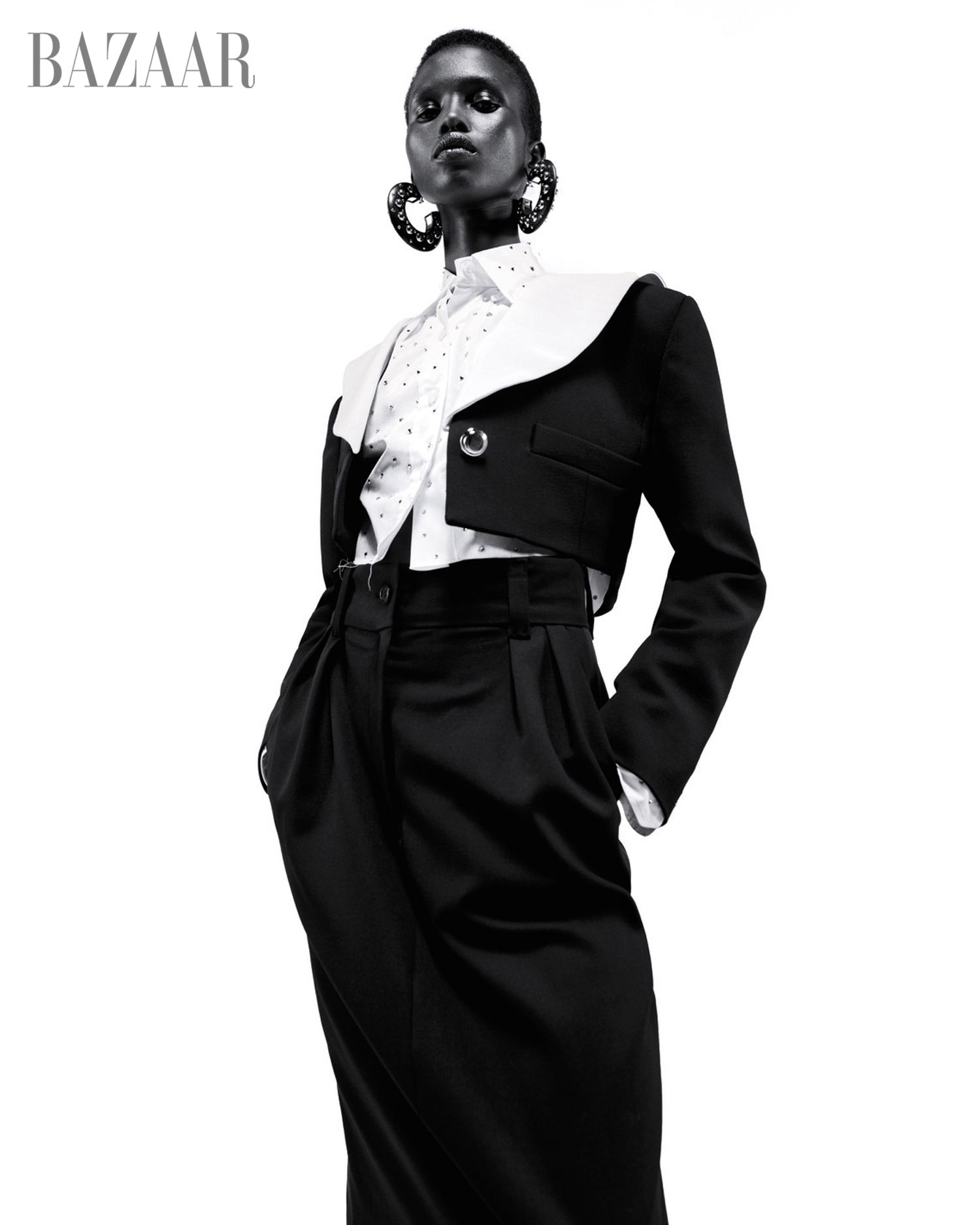 model akway in white dotted collared shirt and black cropped suit jacket and black trousers black and white with white background