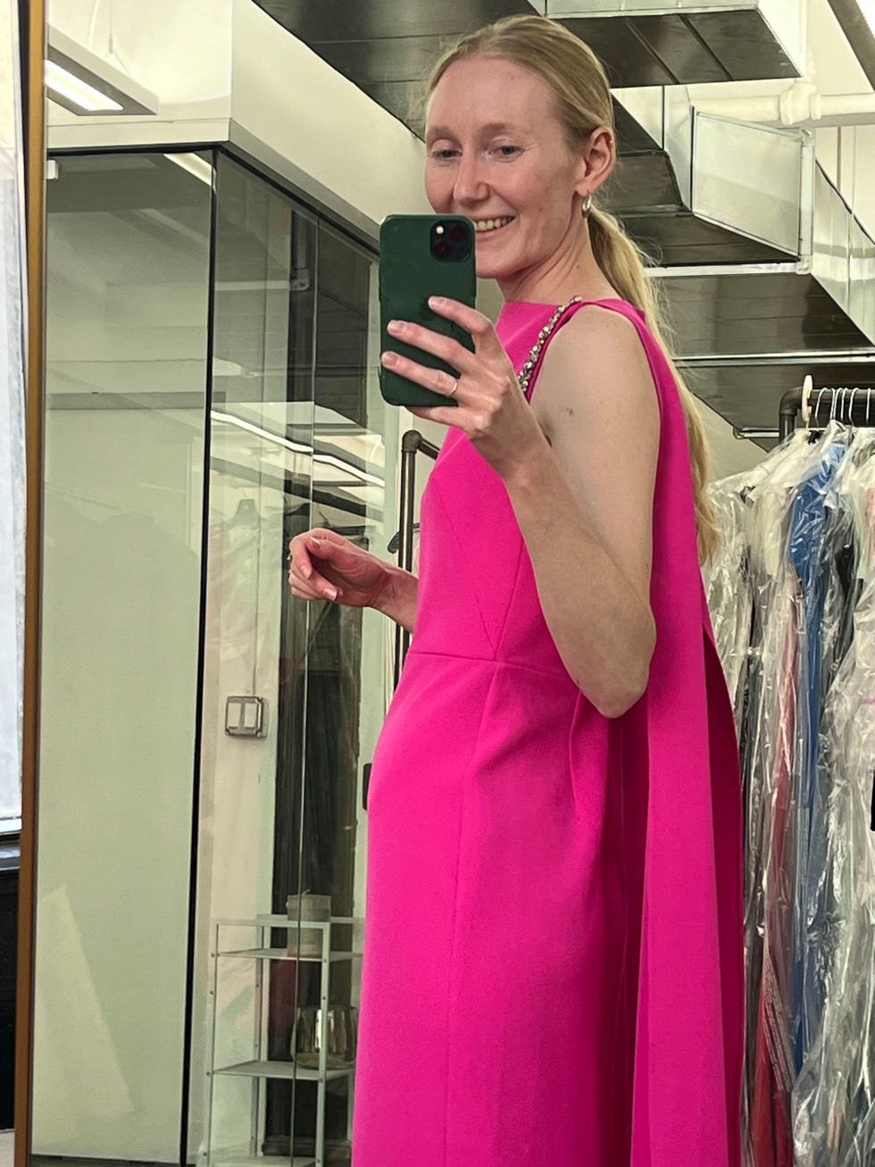 a person wearing a bright pink dress with a cape in a fitting room