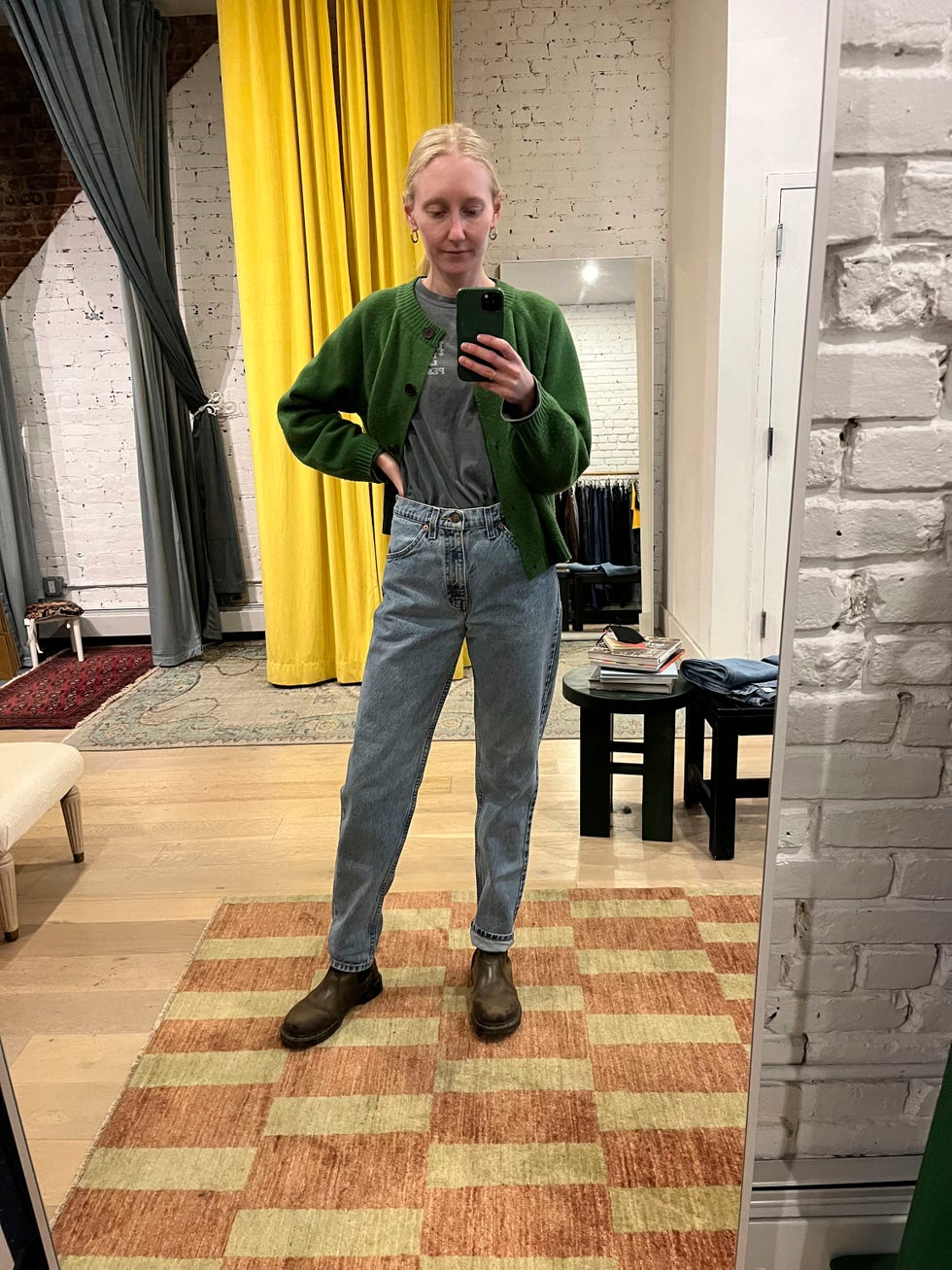 person standing in a clothing store fitting room wearing a green cardigan and highwaisted jeans