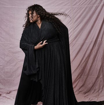 Black flowing garment worn by a person with curly hair against a pink backdrop Black flowing garment worn by a person with curly hair against a pink backdrop