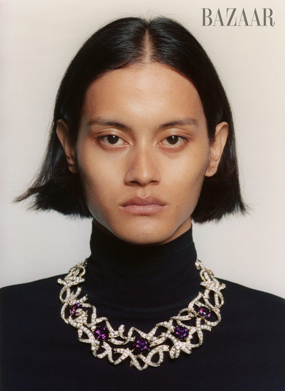 a person wearing an elegant necklace with purple and clear gems against a neutral background