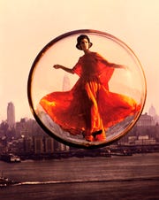 a woman in an orange dress poses in a bubble floating above new york