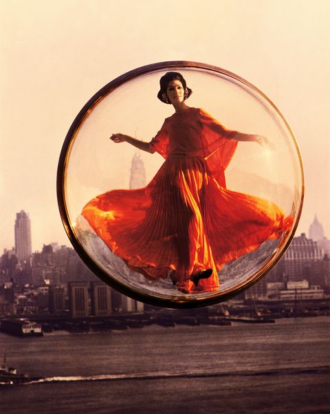 a model in an orange 1960s dress hovers above new york city in a clear bubble in a groundbreaking harper's bazaar shoot by melvin sokolsky