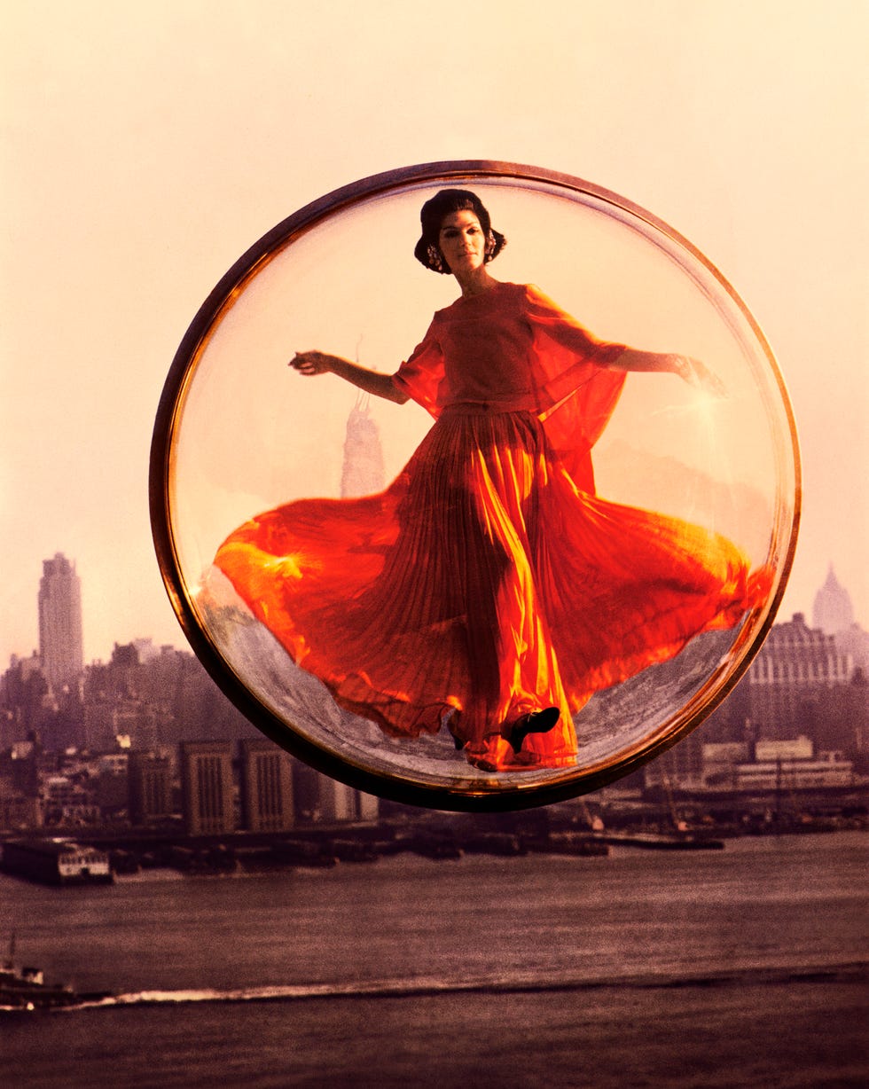 a model in an orange 1960s dress hovers above new york city in a clear bubble in a groundbreaking harper's bazaar shoot by melvin sokolsky