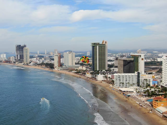 a beach with buildings and a body of water with a hot air balloon in the air