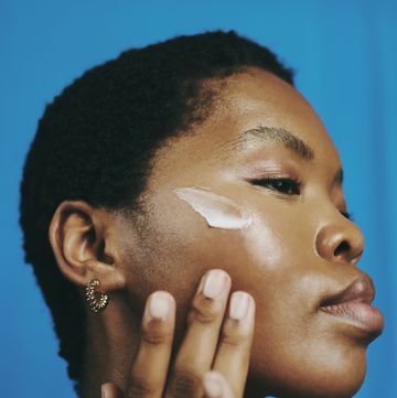 headshot of a beautiful black woman, looking down and thinking as she applies moisturizer to her face with her head tilted backwards, stock photo