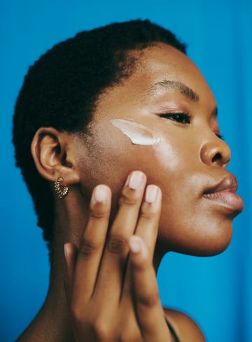 headshot of a beautiful black woman, looking down and thinking as she applies moisturizer to her face with her head tilted backwards, stock photo