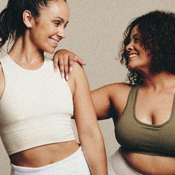 two mixed race women in activewear looking at one another and smiling one has an athletic body shape and the other is curvier