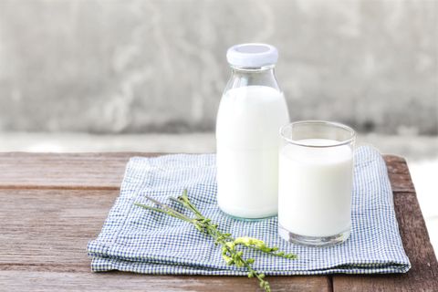 a cup and bottle of milk on a table, an ingredient in one of good housekeeping's best homemade face scrubs
