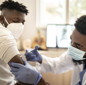 healthcare worker, wearing protective workwear and protective face mask while injecting the covid 19 vaccine, to a responsible male patient