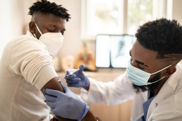 healthcare worker, wearing protective workwear and protective face mask while injecting the covid 19 vaccine, to a responsible male patient