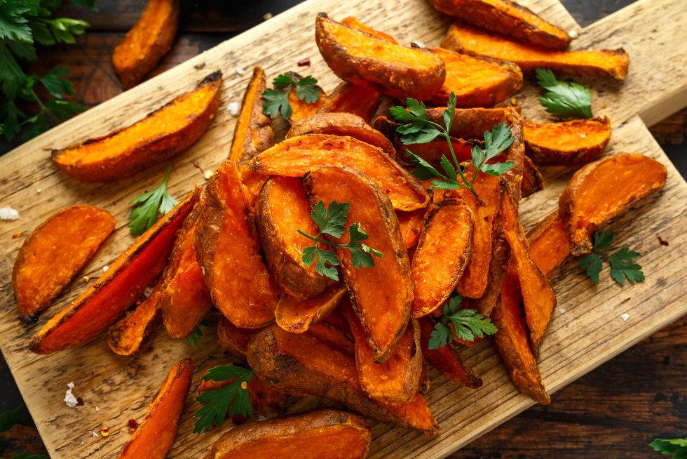 healthy baked orange sweet potato wedges with dip sauce, herbs, salt and pepper on wooden board what to eat after gym
