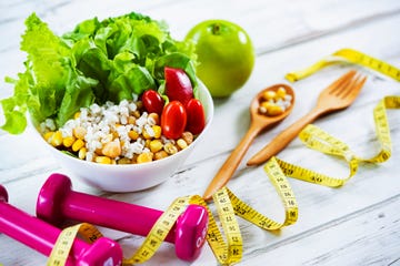healthy eating and exercising with fresh healthy salad and dumbbells and tape measure