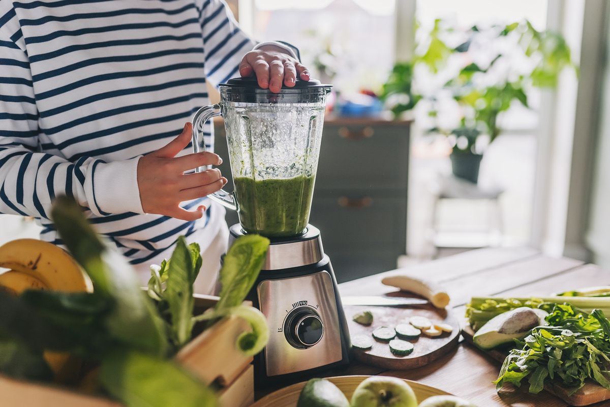 healthy eating, cooking, vegetarian food, dieting and people concept close up of young woman with blender and green vegetables making detox shake or smoothie at home
