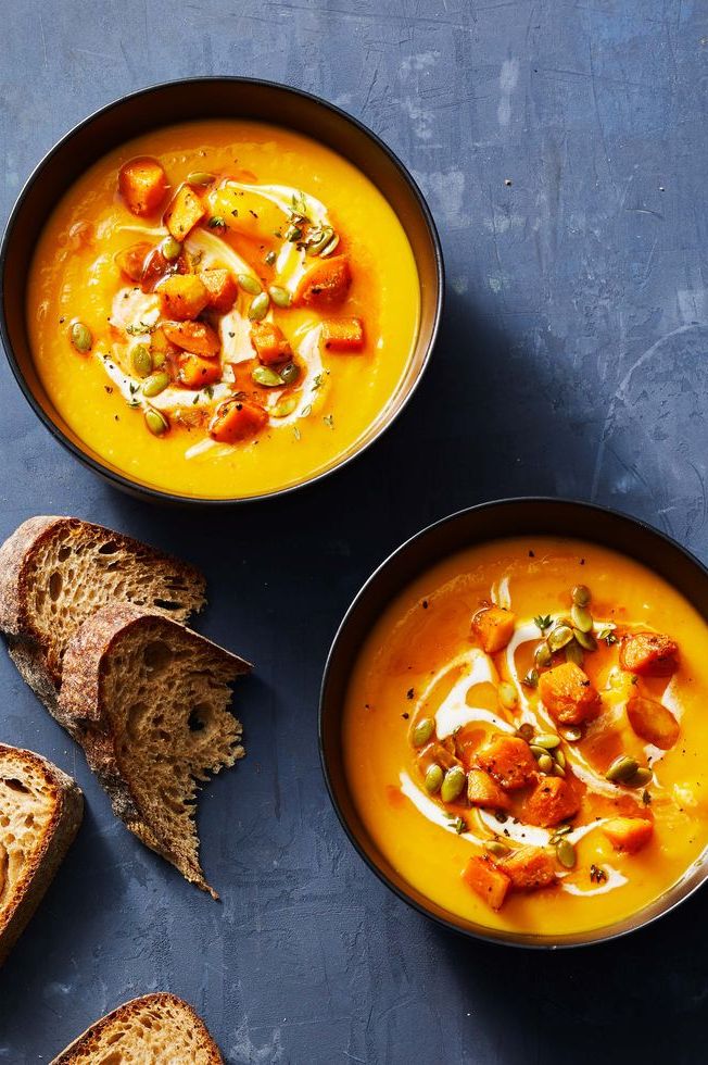 two bowls of butternut squash soup with a side of bread