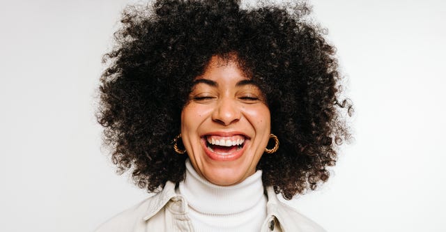 happy woman with curly hair laughing cheerfully while standing against a white background beautiful young woman of colour wearing her natural hair with pride