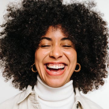 Woman with curly hair laughing happily in a studio happy woman with curly hair laughing cheerfully while standing against a white background beautiful young woman of colour wearing her natural hair with pride