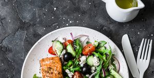 healthy mediterranean lunch   grilled fillet salmon and vegetables, olives, feta greek salad on dark background, top view