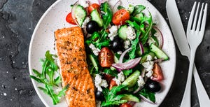 healthy mediterranean lunch   grilled fillet salmon and vegetables, olives, feta greek salad on dark background, top view