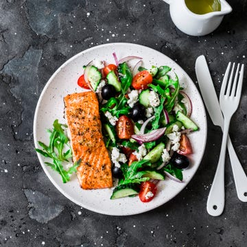 healthy mediterranean lunch   grilled fillet salmon and vegetables, olives, feta greek salad on dark background, top view