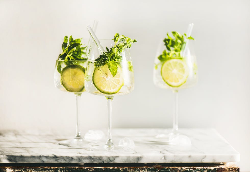 hugo sparkling wine cocktail with fresh mint and lime in glasses with eco friendly straws over white marble counter, selective focus. cold refreshing summer alcoholic drink