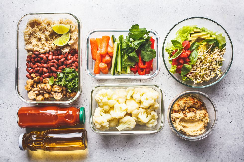 healthy vegan food in glass containers, top view rice, beans, vegetables, hummus and juice